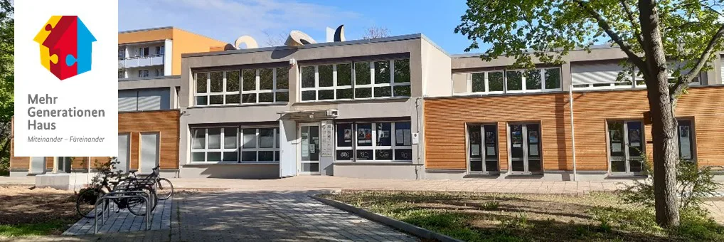 Das Gebäude von Mehrgenerationenhaus Pusteblume ist ein zweistöckiger Bau, grau verputzt, im Erdgeschoß holzverkleidet, mit großen Fenster-Türen. Vor dem Haus kann man sich aufhalten, einen Fahrradständer gibt es auch