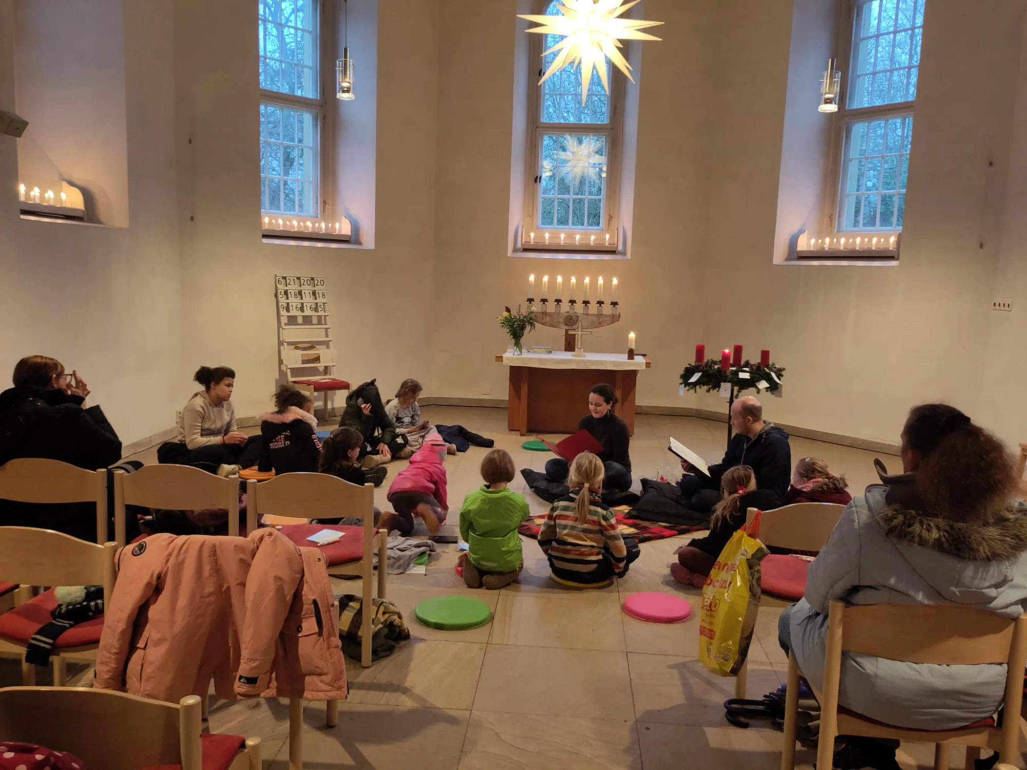 In der Kirche sitzen Kinder auf bunten Kissen auf dem Boden. Es scheint als würde ein Buch vorgelesen werden.