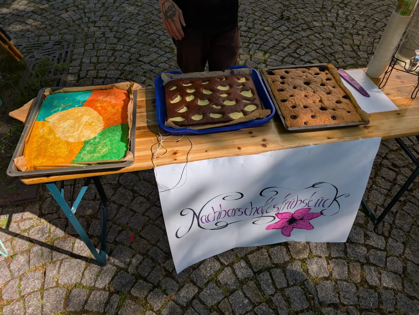 Ein Tisch mit 3 Kuchen und einem Schild auf dem steht nachbarschaftsfrühstück